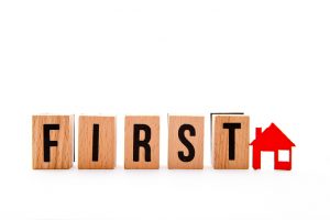 First Home - wooden block letters and red home icon on white background